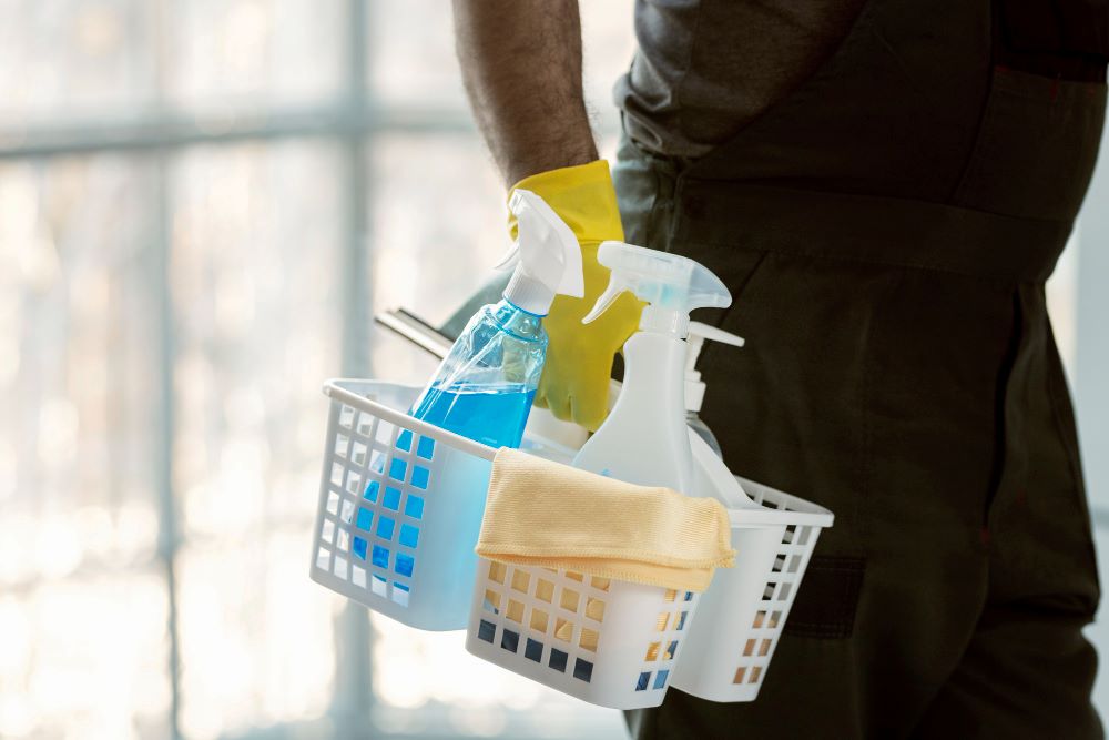 Cleaner in yellow glove holding a basket of cleaning supplies
